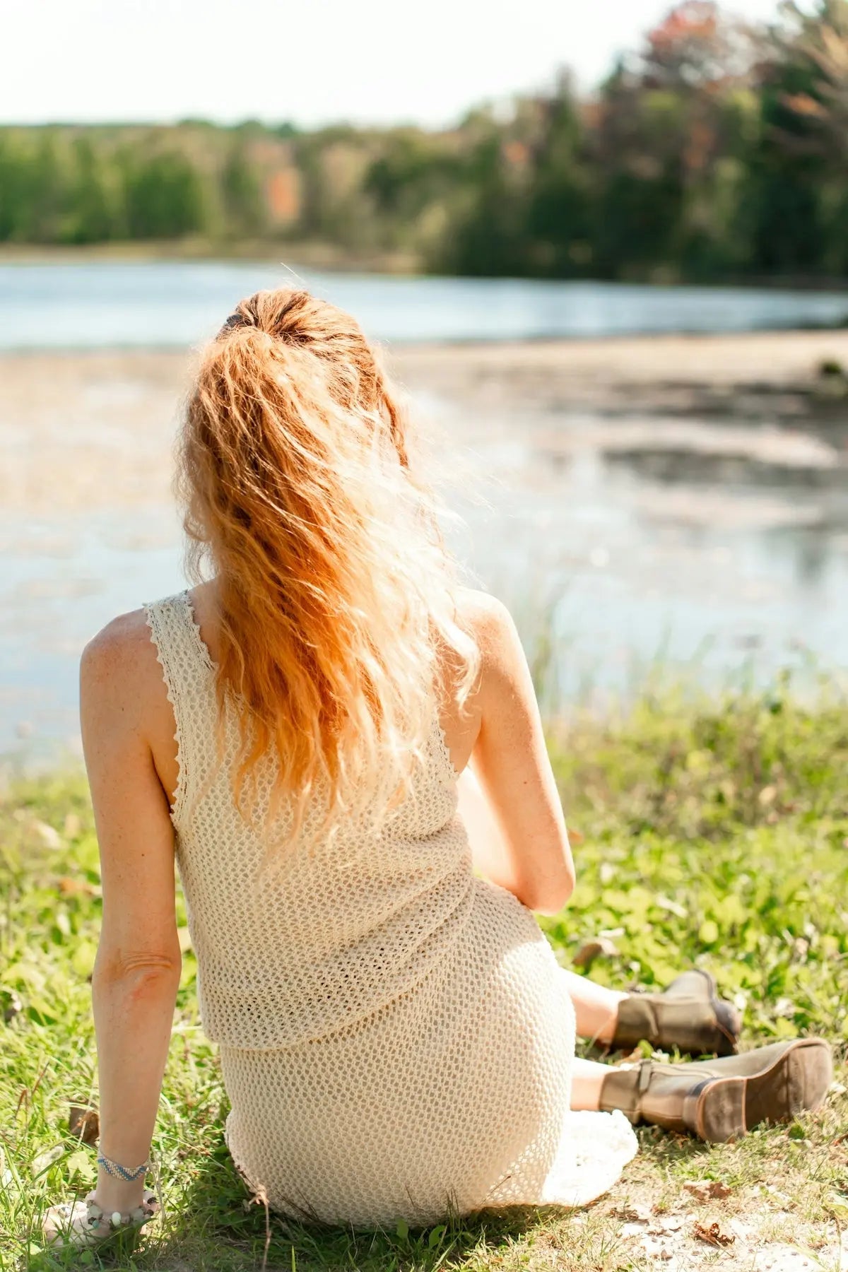 A woman is sitting on the grass by the water