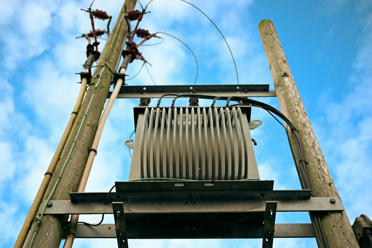 Electrical transformer mounted on wooden poles against sky