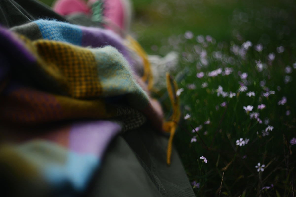 Colorful blanket draped over camping gear near wildflowers.