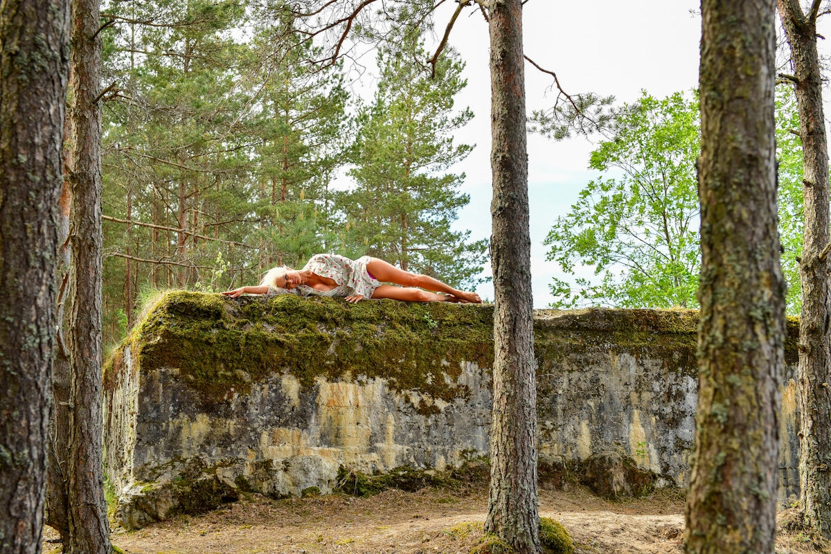 Woman resting on moss-covered concrete structure in forest.