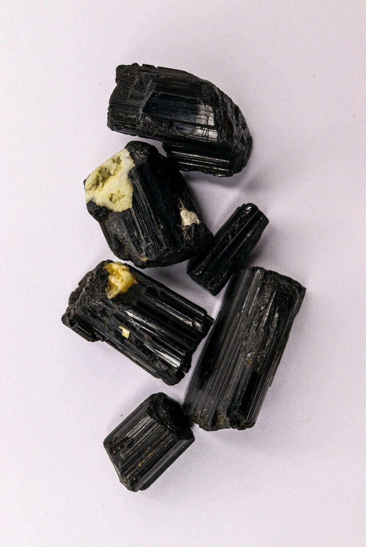 Rough black tourmaline crystals on a white surface.