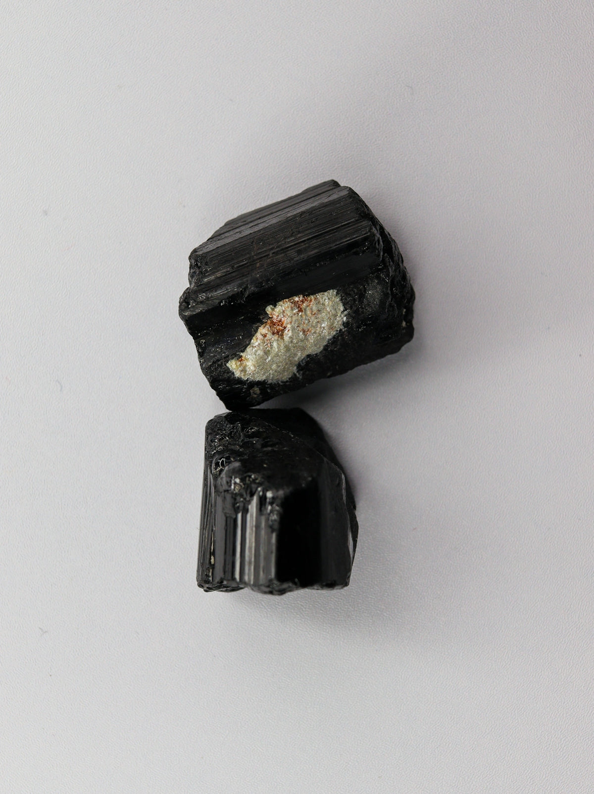 Two black mineral pieces with white inclusion on white background.
